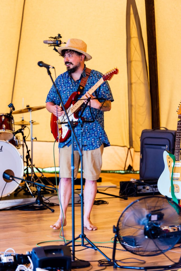 Picture of Matt Barber playing the guitar wearing a blue shirt and tan shorts